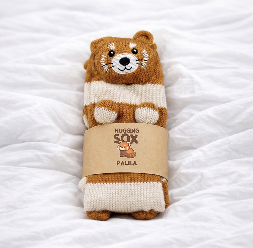 HuggingSox - Paula der rote Panda Socken auf einer Decke mit Verpackung